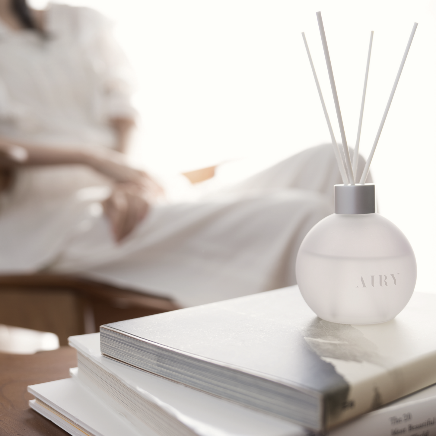 Blissful Harmony 悦 displayed on a stack of art books in a bright, modern living room. The frosted glass vessel and white reeds represent a minimalist Japanese aesthetic, ideal for luxury home decor and refined British interiors.