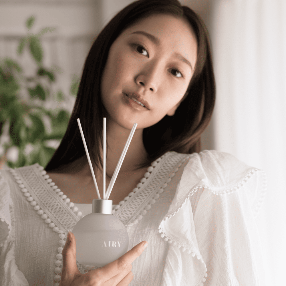Sophisticated lifestyle portrait of a woman holding the Blissful Harmony 悦 reed diffuser. The image showcases the frosted glass vessel and white reeds against a minimalist backdrop, highlighting the elegant and airy aesthetic of this luxury Japanese home fragrance.