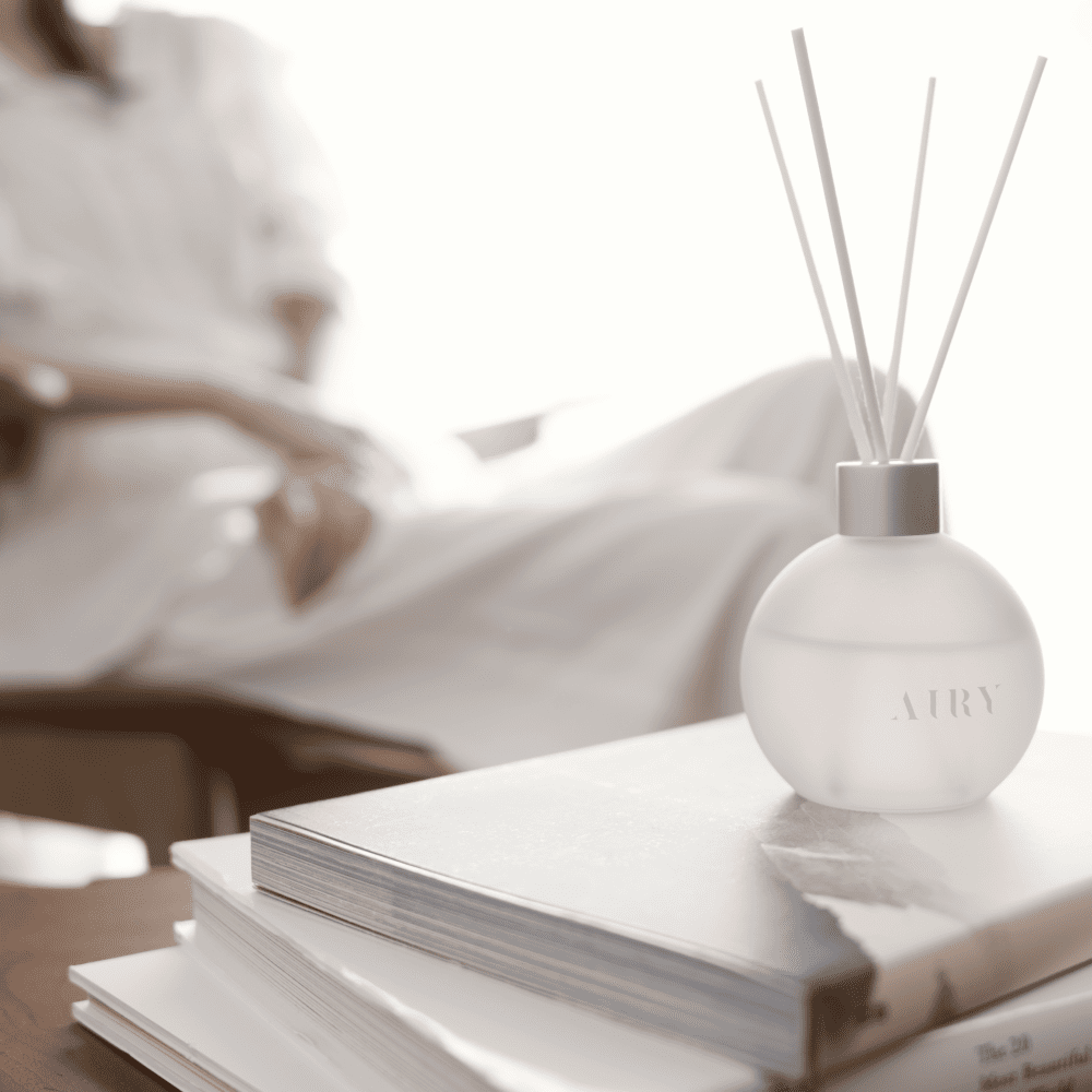 Elegant Harmony 優 reed diffuser displayed on a stack of art books in a bright, modern living room. The frosted glass vessel and white reeds represent a minimalist Japanese aesthetic, ideal for luxury home decor and refined British interiors.