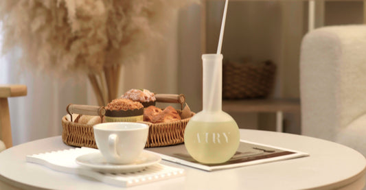 AIRY® Fragrances reed diffuser on a coffee table beside a ceramic cup, pastries, and a magazine in a warm minimal living room, evoking the Japanese ikigai philosophy of small daily pleasures at home.
