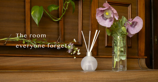 AIRY® Fragrances reed diffuser on a wooden console beside fresh pink poppies and trailing green leaves, styled as a considered home entrance,  luxury home fragrance by AIRY® Fragrances.