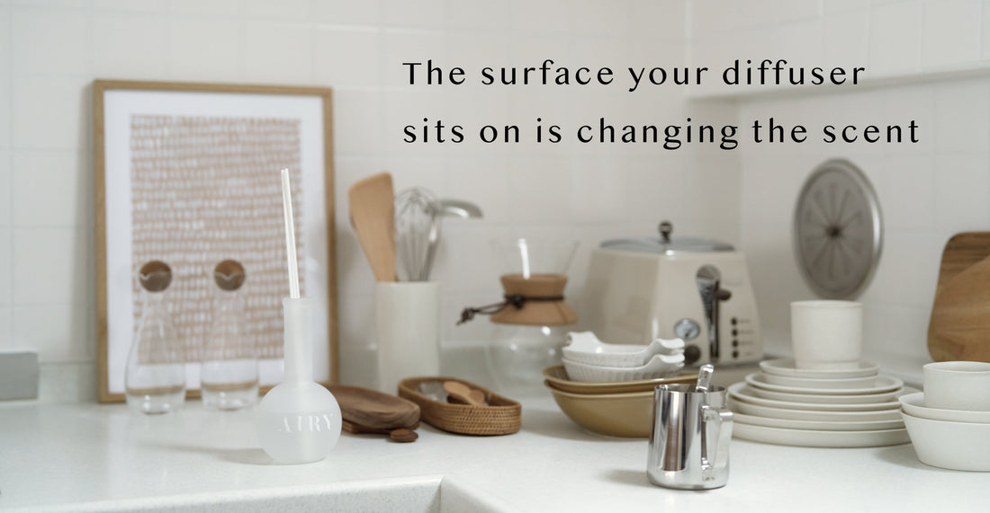 AIRY® Fragrances reed diffuser on a white kitchen surface surrounded by ceramic dishes, wooden utensils, and natural materials, evoking how different surfaces interact with home fragrance.