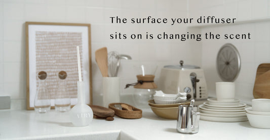 AIRY® Fragrances reed diffuser on a white kitchen surface surrounded by ceramic dishes, wooden utensils, and natural materials, evoking how different surfaces interact with home fragrance.