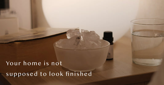 AIRY® Fragrances clear quartz crystal stone diffuser in a raw ceramic bowl on a wooden surface, styled with a glass of water and fragrance oil bottle in warm low light,  wabi-sabi inspired home fragrance by AIRY® Fragrances. 