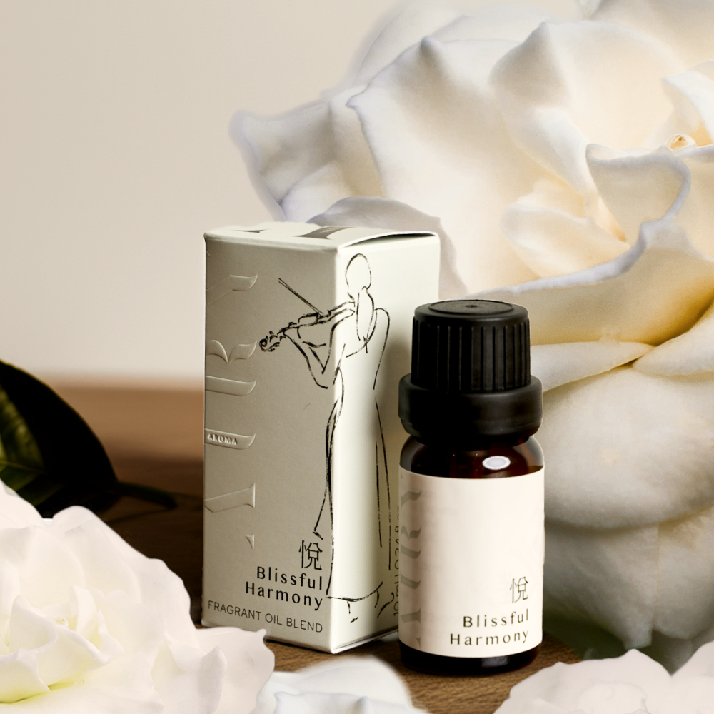Blissful Harmony 悦 (Etsu) luxury fragrant oil styled with fresh white gardenia flowers. The 10ml amber bottle and minimalist box featuring a violin illustration are shown in a soft, botanical setting. A Japanese-crafted, alcohol-free green tea and gardenia scent designed for the Airy Stone Diffuser ritual to evoke joy and mental clarity.