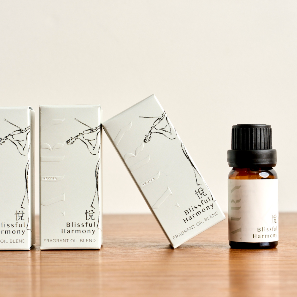 Airy Fragrances Blissful Harmony 悦 (Etsu) fragrant oil range on a wooden surface. Features a single 10ml amber bottle with one of its minimalist white boxes open, showcasing the elegant black botanical drawing. This Japanese-crafted, alcohol-free blend of green tea and gardenia is an Editor's Pick from The Guardian, designed for use with the Airy Stone Diffuser ritual.
