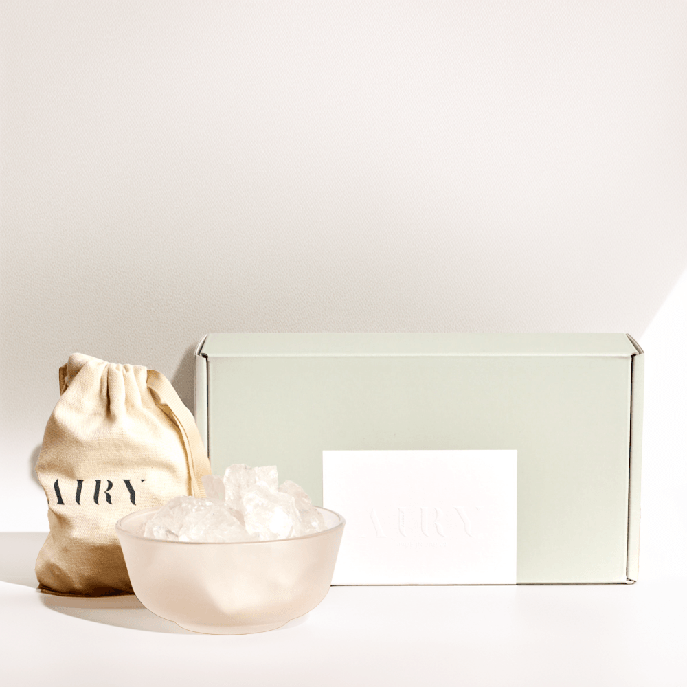 Airy Fragrances luxury Stone Diffuser Set, an Editor’s Pick featured in The Guardian and Ideal Home. Image shows the complete minimalist unboxing experience: a frosted round glass container, 500g of raw natural Clear Quartz stones in a signature cotton drawstring bag, and premium gift packaging. 100% natural Japanese-crafted wellness set for mental clarity and minimalist home decor.