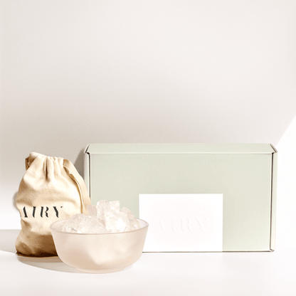 Airy Fragrances luxury Stone Diffuser Set, an Editor’s Pick featured in The Guardian and Ideal Home. Image shows the complete minimalist unboxing experience: a frosted round glass container, 500g of raw natural Clear Quartz stones in a signature cotton drawstring bag, and premium gift packaging. 100% natural Japanese-crafted wellness set for mental clarity and minimalist home decor.