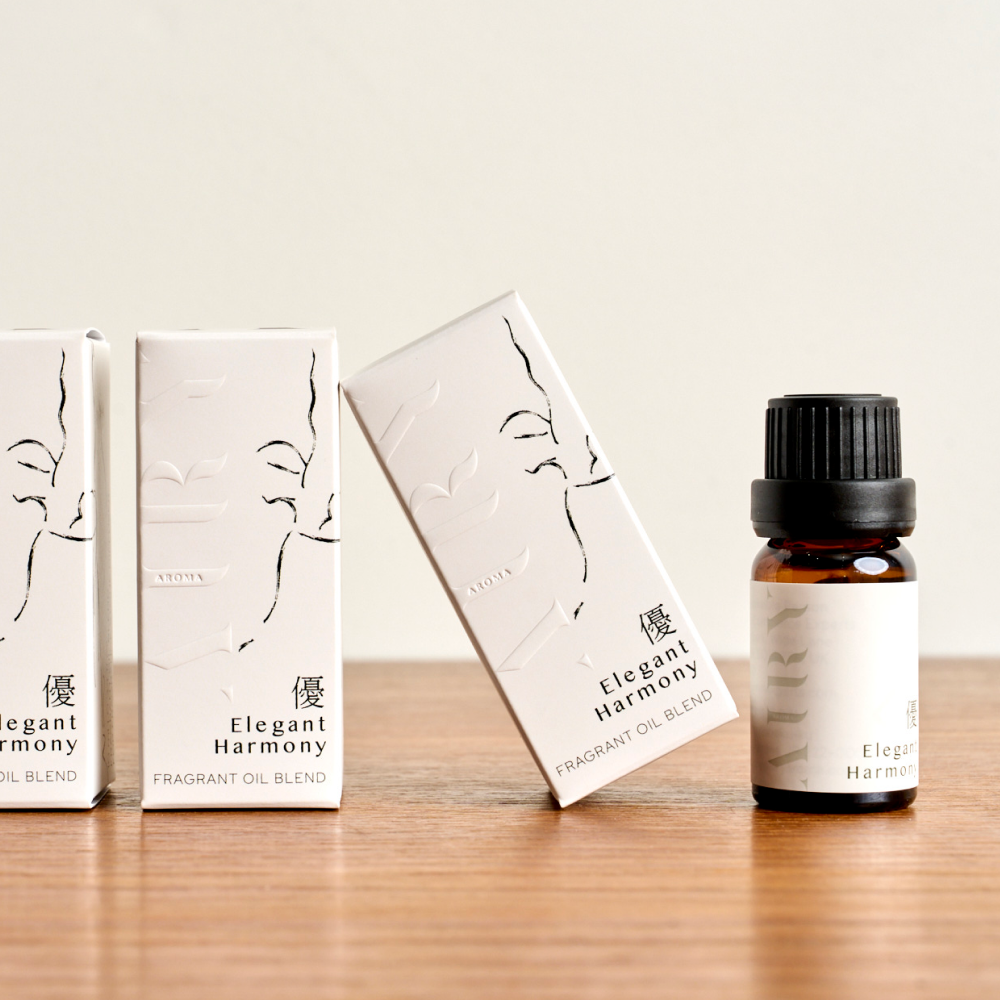 Airy Fragrances Elegant Harmony 優 (Yu) fragrant oil range displayed on a wooden surface. Features the 10ml amber glass bottle alongside its minimalist white packaging with elegant black line art. This Japanese-crafted, alcohol-free blend of white tea and osmanthus is a sophisticated choice for stone diffusion rituals, offering a sense of quiet confidence and grace