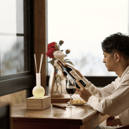 Masculine luxury lifestyle setting for Forest Breath 森 reed diffuser. A man in a refined interior enjoying a glass of wine, with the Nagano Hinoki diffuser prominently displayed. This visual reinforces the woody, grounding character of the scent, making it a perfect gift for men and sophisticated dens or home offices