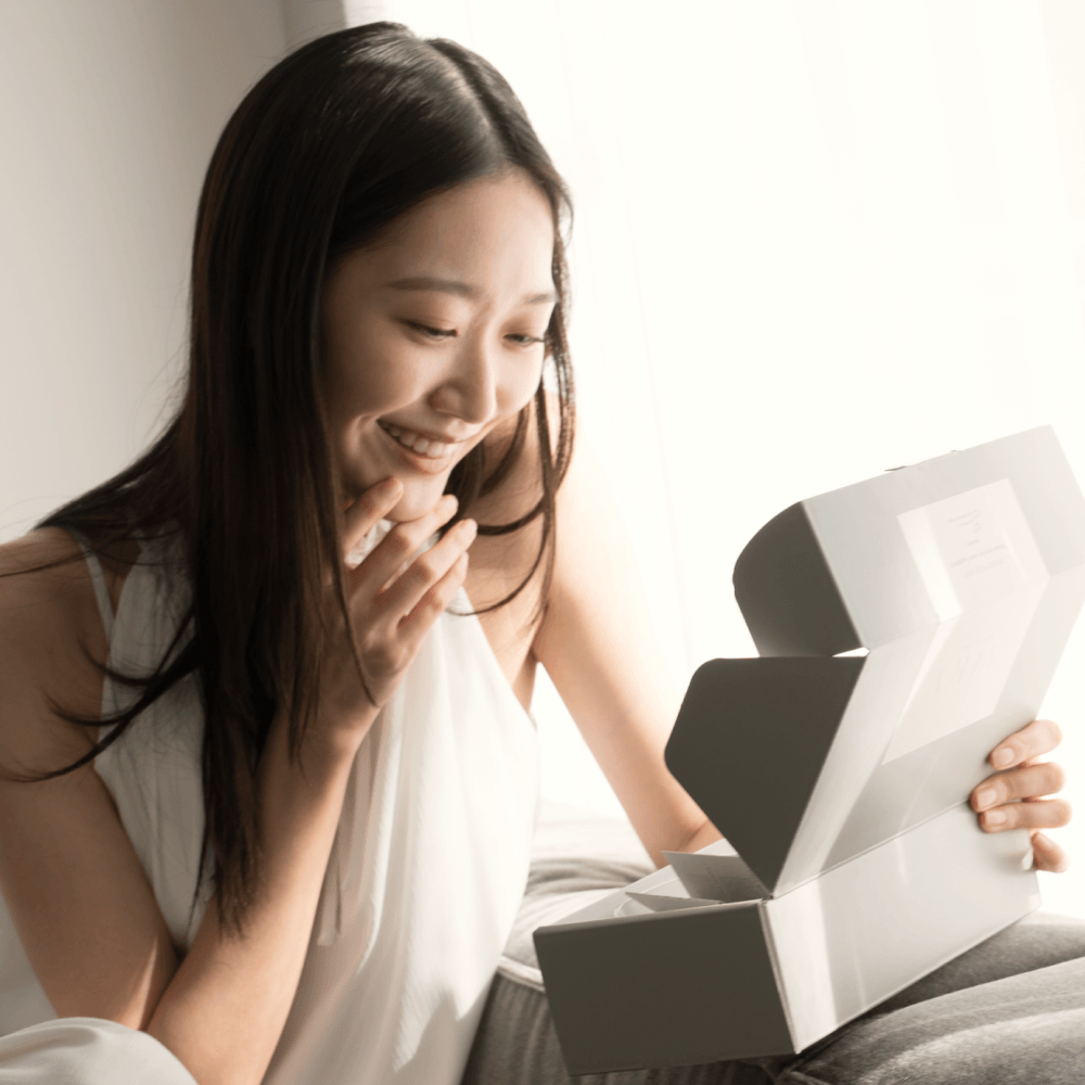 Lifestyle image of a woman happily unboxing the Airy Fragrances Clear Quartz Stone Diffuser set. This premium Japanese-crafted wellness gift features minimalist sustainable packaging, making it an ideal choice for housewarmings, birthdays, or a 'New Home' blessing for those seeking mental clarity and Zen home decor.