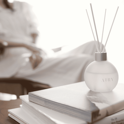 Elegant Harmony 優 reed diffuser displayed on a stack of art books in a bright, modern living room. The frosted glass vessel and white reeds represent a minimalist Japanese aesthetic, ideal for luxury home decor and refined British interiors.