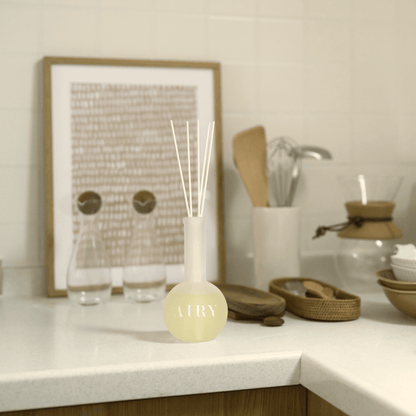 Forest Breath 森 reed diffuser displayed in a modern minimalist kitchen setting. The frosted glass vessel and white fiber reeds complement the clean, natural wood and stone textures, highlighting the Hinoki scent’s ability to refresh and clear the air in sophisticated culinary spaces.