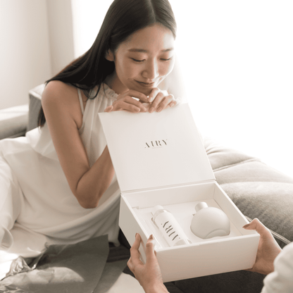 A woman opening the luxury white gift box of the Blissful Harmony 悦 reed diffuser set. The image shows the premium presentation of the frosted glass vessel and fragrance oil bottle, perfect for high-end Japanese gifting for housewarmings or special occasions.