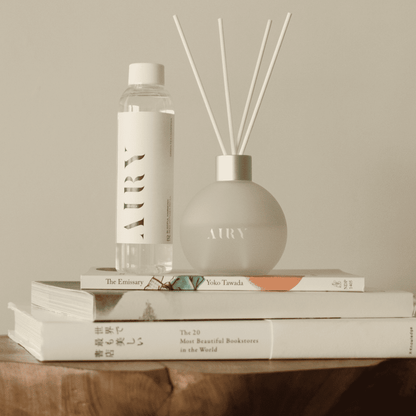 Minimalist Japanese home decor featuring Blissful Harmony 悦 reed diffuser set on a stack of books. Elegant frosted glass vessel and fragrance oil refill on a wooden table, representing a quiet, calm living space aesthetic
